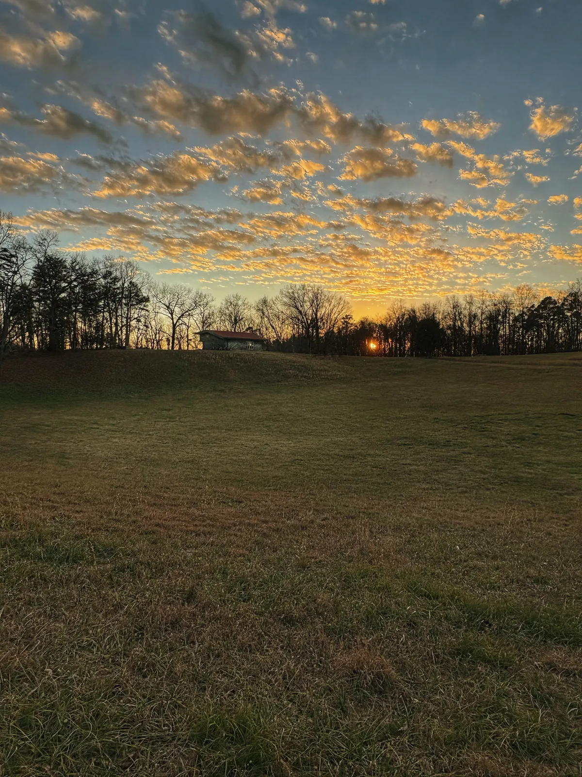 The barn at Hickory Hill Farm on its ridge above a wide field, the sun setting behind the treeline