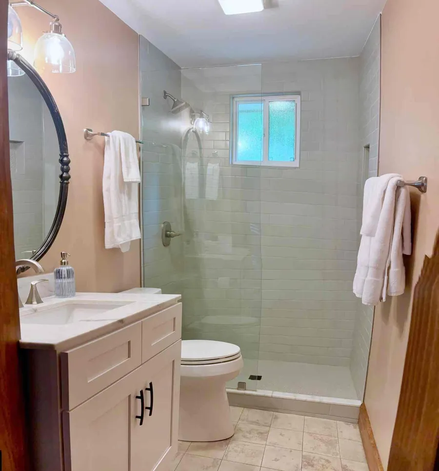 The bathroom with a round mirror over the vanity and a glassed walk-in shower