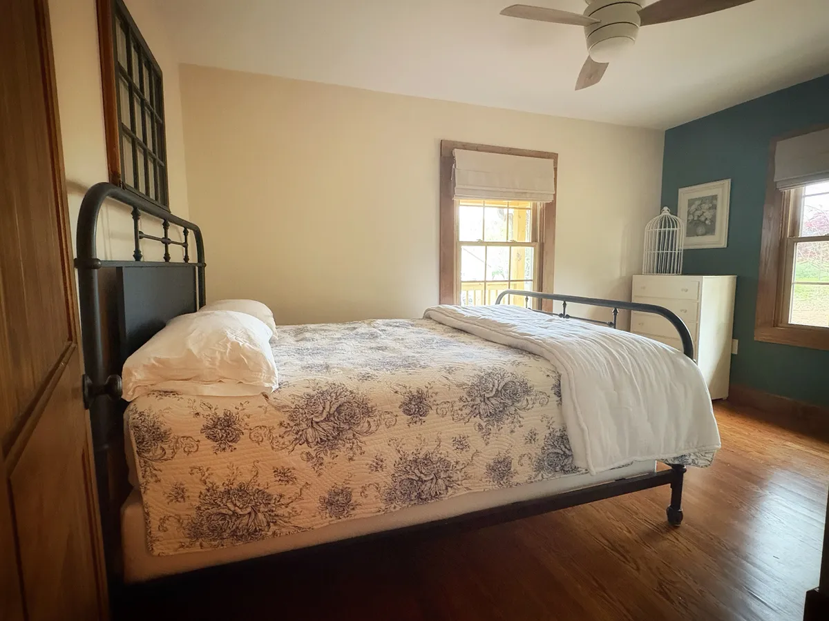 A bedroom made up, black iron bedstead on hardwood with the window alongside