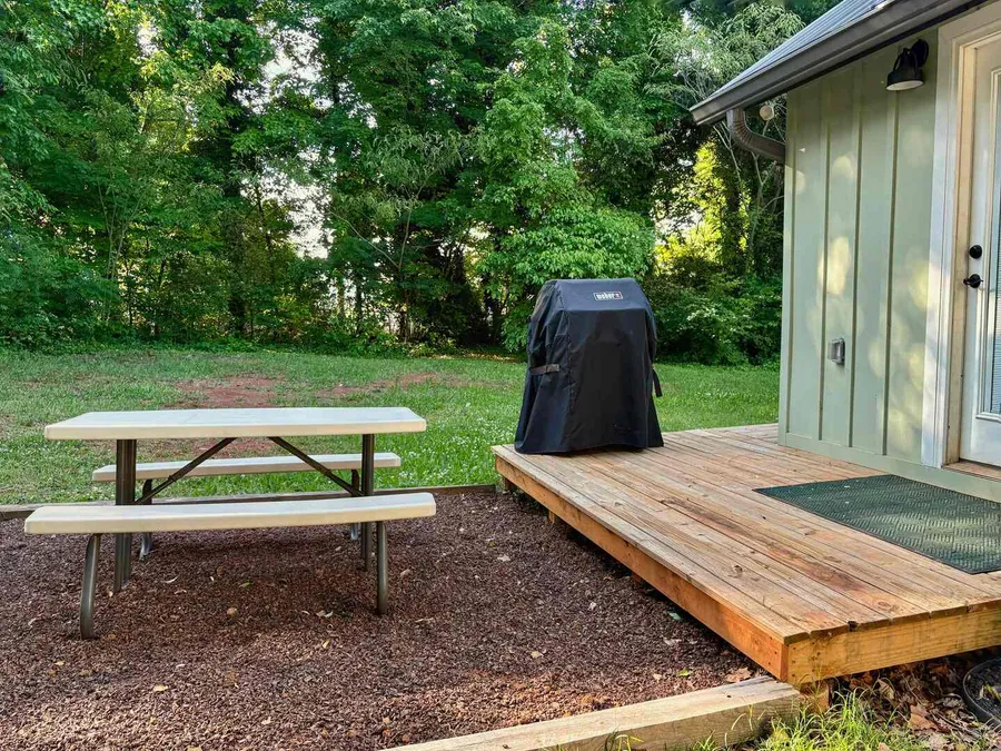 A picnic table and a covered grill on the grass beside the cottage deck