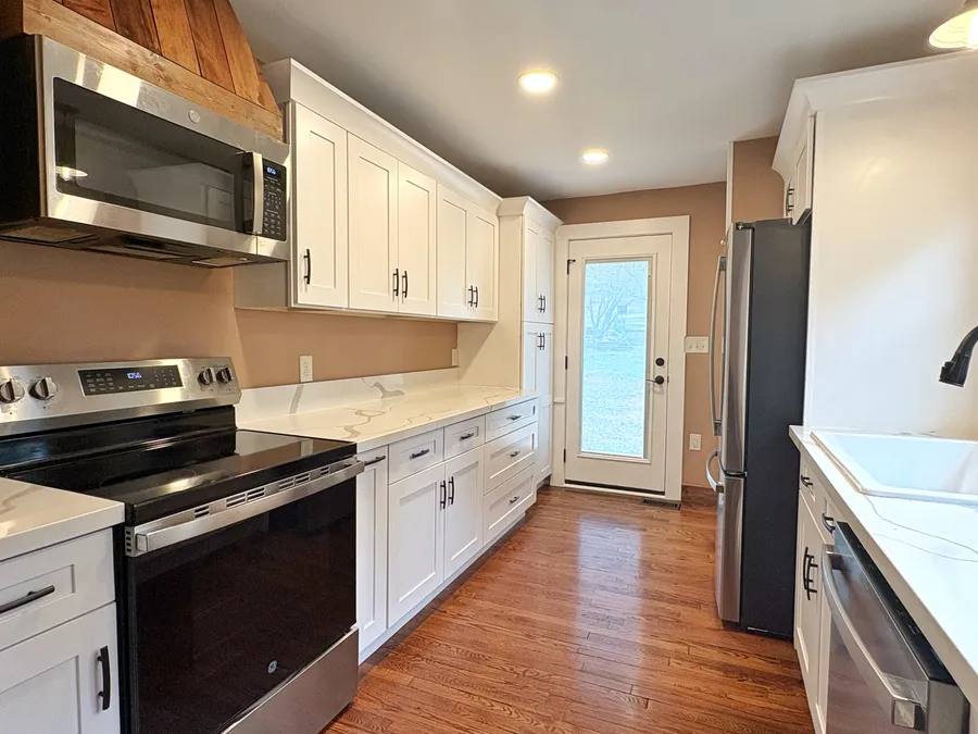 The kitchen with white cabinets, a range under a wooden hood, and a glazed door to outside