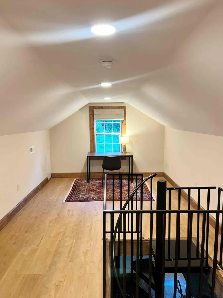 A desk and chair set under the loft window, the spiral stair rail in the foreground